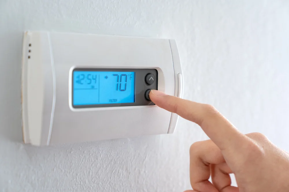 Homeowner adjusting a programmable wall thermostat set to 70 degrees